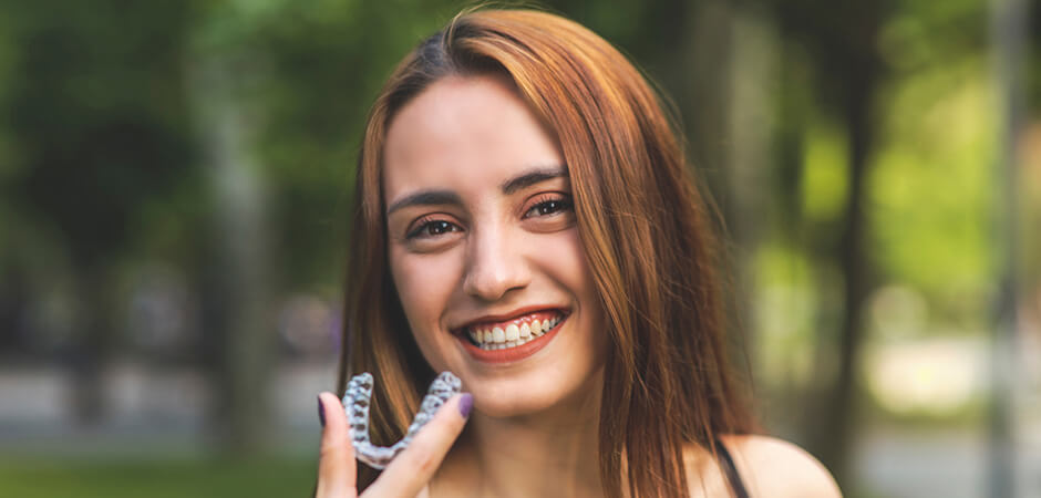 Young Smiling Woman holding up Invisalign Bracer